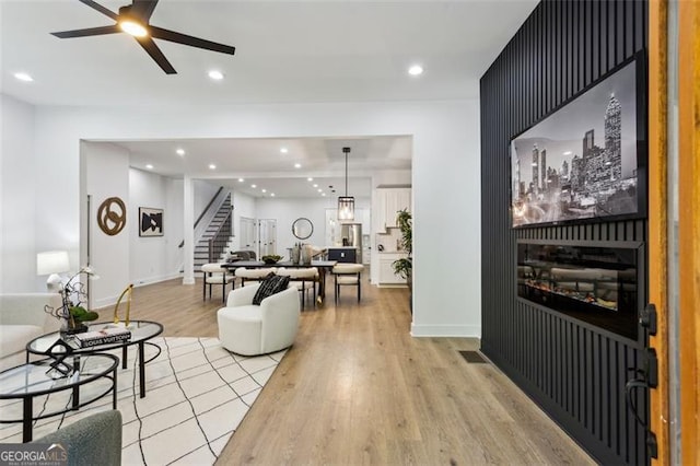 living area featuring ceiling fan, recessed lighting, baseboards, light wood-type flooring, and stairway