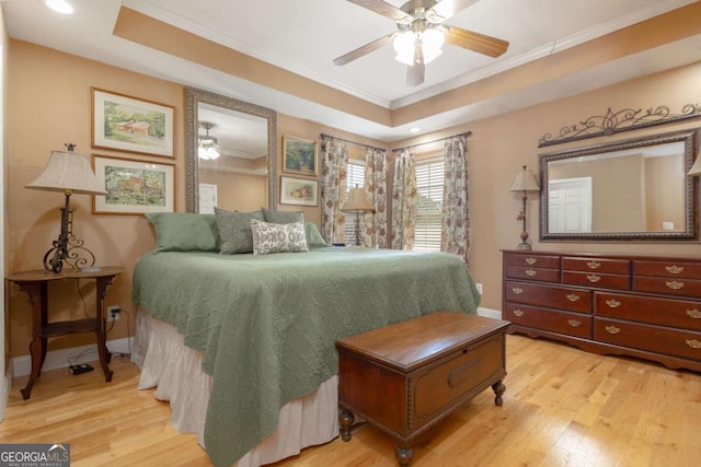 bedroom with ornamental molding, baseboards, ceiling fan, light wood-type flooring, and a tray ceiling