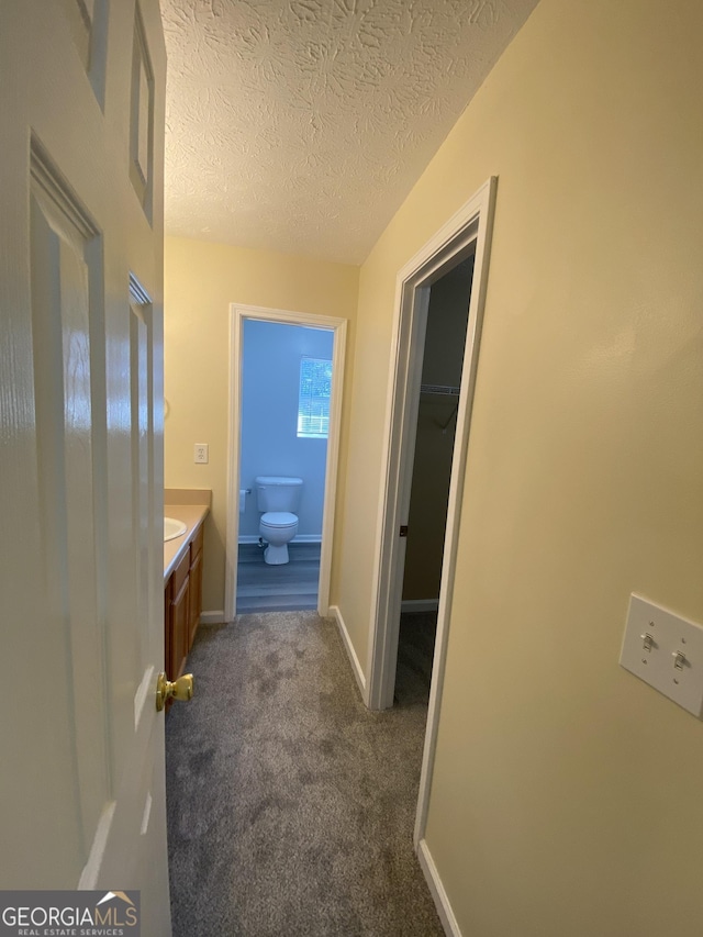 hall with baseboards, dark colored carpet, and a textured ceiling