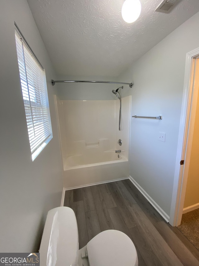 full bath with visible vents, wood finished floors, toilet, washtub / shower combination, and a textured ceiling
