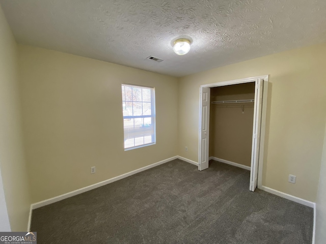 unfurnished bedroom with a textured ceiling, visible vents, baseboards, a closet, and dark colored carpet
