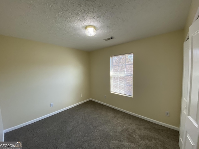 spare room with a textured ceiling, baseboards, visible vents, and dark colored carpet