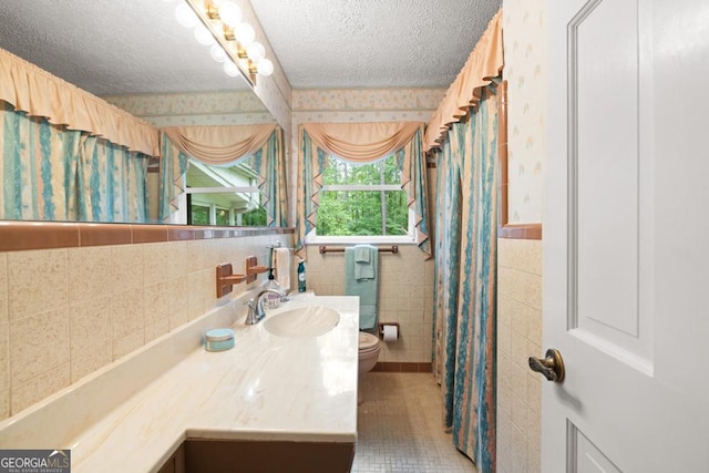 bathroom featuring vanity, toilet, a textured ceiling, wallpapered walls, and tile walls