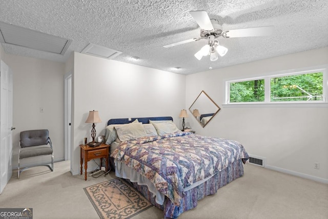 carpeted bedroom with ceiling fan, a textured ceiling, attic access, baseboards, and visible vents