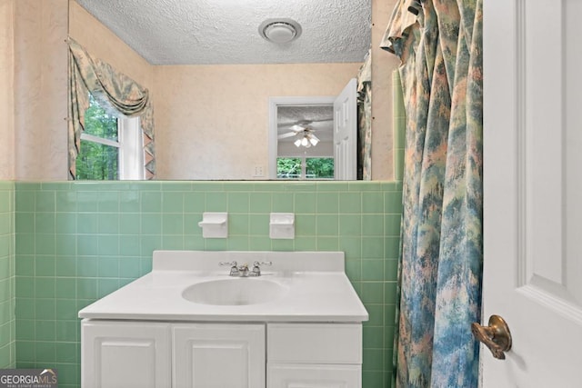 full bathroom with vanity, a ceiling fan, a textured ceiling, and tile walls