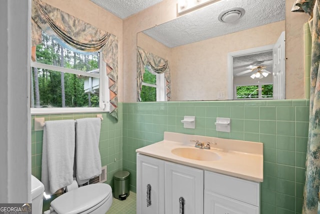 bathroom featuring a textured ceiling, a wealth of natural light, toilet, and tile walls