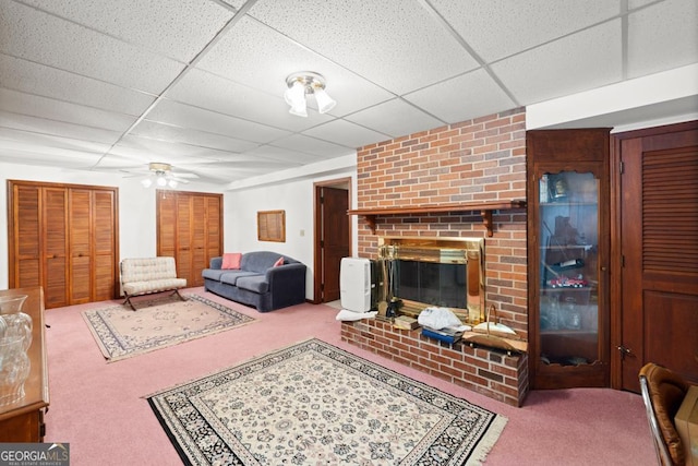 living area with carpet floors, a ceiling fan, a drop ceiling, and a fireplace