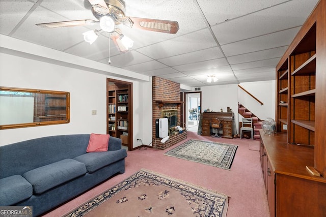 living area with a brick fireplace, stairway, a paneled ceiling, a ceiling fan, and carpet