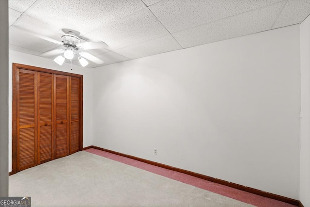 unfurnished bedroom with a closet, baseboards, ceiling fan, a paneled ceiling, and carpet flooring
