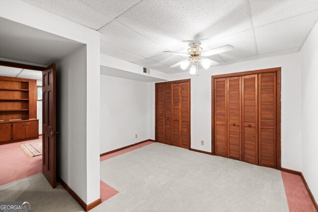 unfurnished bedroom with visible vents, two closets, baseboards, a drop ceiling, and carpet flooring