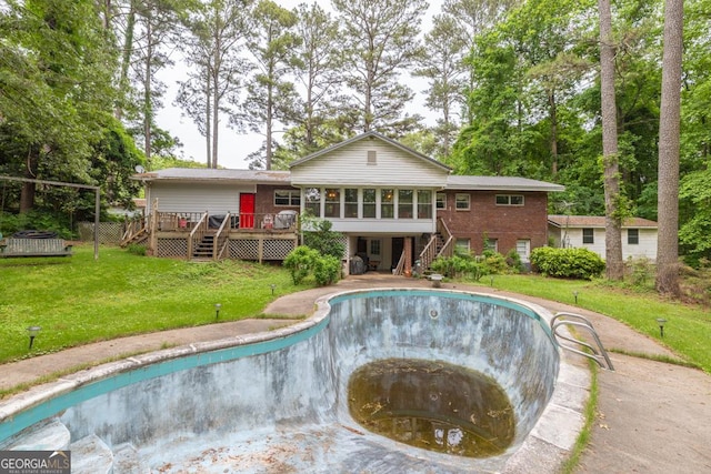 back of property featuring stairs, a wooden deck, a sunroom, an empty pool, and a yard