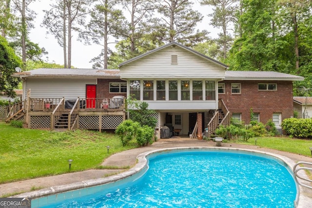 back of house featuring a deck, an outdoor pool, a sunroom, stairway, and brick siding