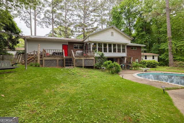 rear view of property featuring a wooden deck, an outdoor pool, a sunroom, a lawn, and stairway