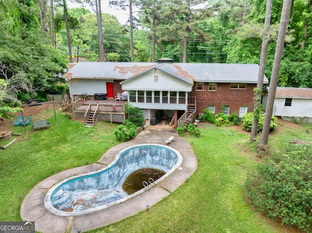 rear view of house featuring a wooden deck, an empty pool, a sunroom, brick siding, and stairway