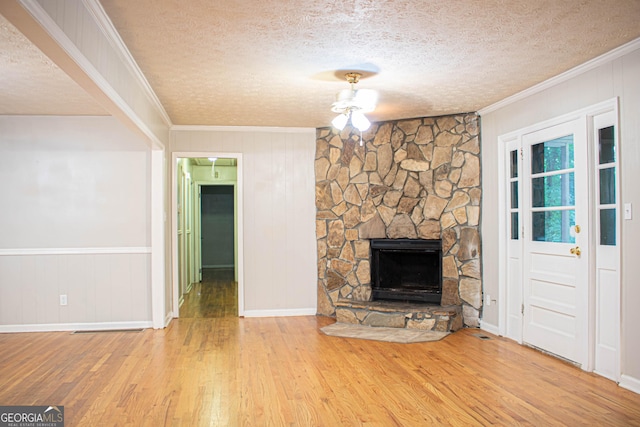 unfurnished living room featuring crown molding, wood walls, wood finished floors, a stone fireplace, and a textured ceiling