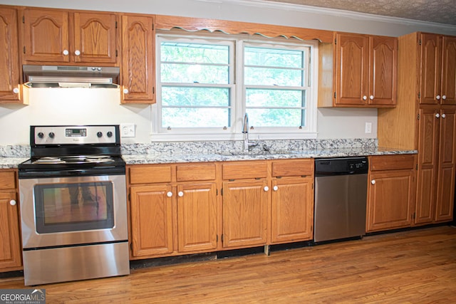 kitchen featuring crown molding, light stone countertops, under cabinet range hood, a sink, and stainless steel appliances