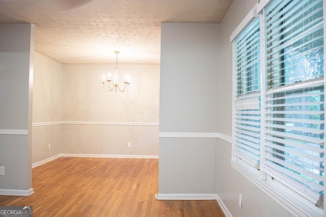 unfurnished dining area featuring an inviting chandelier, a textured ceiling, and wood finished floors