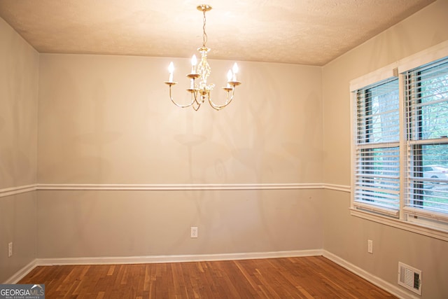 unfurnished dining area featuring a chandelier, a textured ceiling, visible vents, and wood finished floors