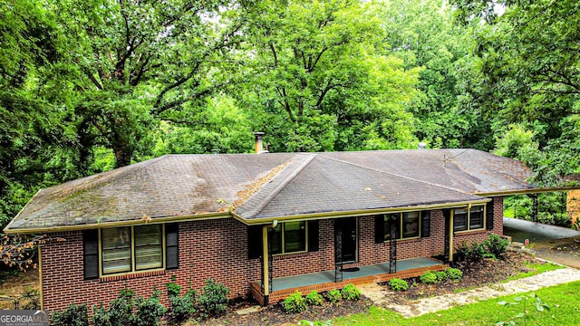 ranch-style house featuring a shingled roof, an attached carport, a porch, and brick siding