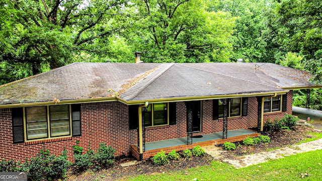 ranch-style home with a shingled roof, a porch, and brick siding