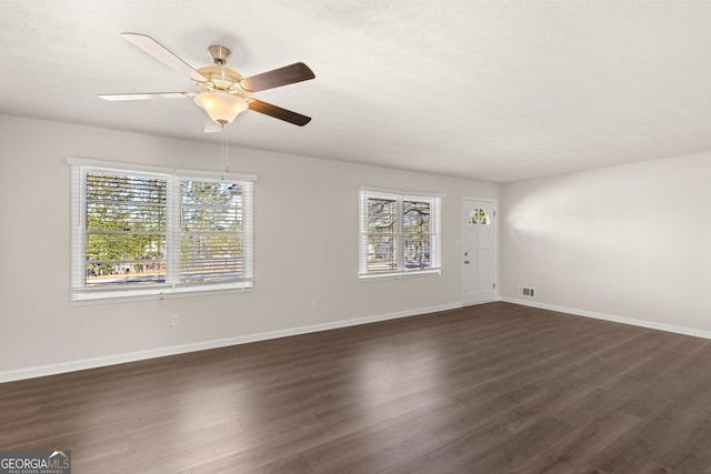 unfurnished room with ceiling fan, visible vents, plenty of natural light, and dark wood-type flooring