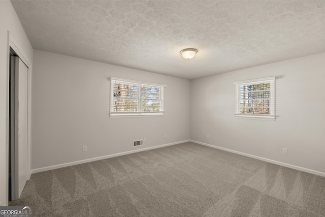 unfurnished bedroom with carpet floors, multiple windows, baseboards, and a textured ceiling