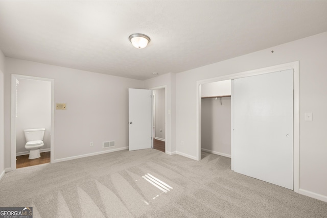 unfurnished bedroom with visible vents, a closet, baseboards, light colored carpet, and ensuite bath