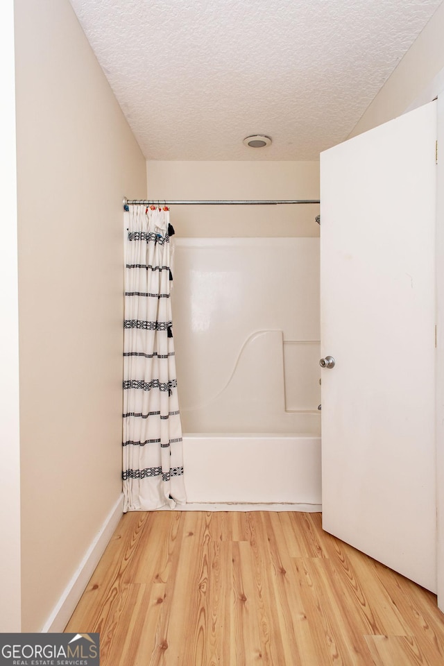 full bath with shower / bath combo with shower curtain, a textured ceiling, and wood finished floors