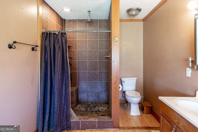 bathroom with vanity, wood finished floors, toilet, tiled shower, and a textured ceiling