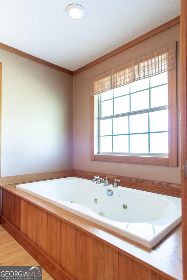 bathroom featuring a jetted tub, ornamental molding, and wood finished floors