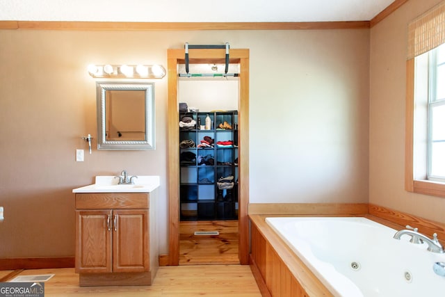 bathroom featuring a tub with jets, a walk in closet, wood finished floors, and vanity