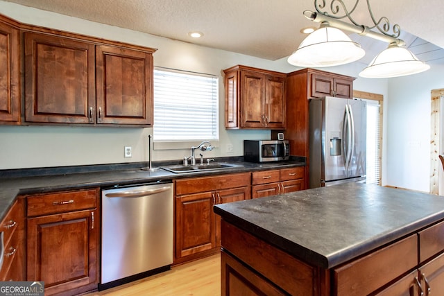 kitchen with dark countertops, light wood-type flooring, a center island, a sink, and appliances with stainless steel finishes