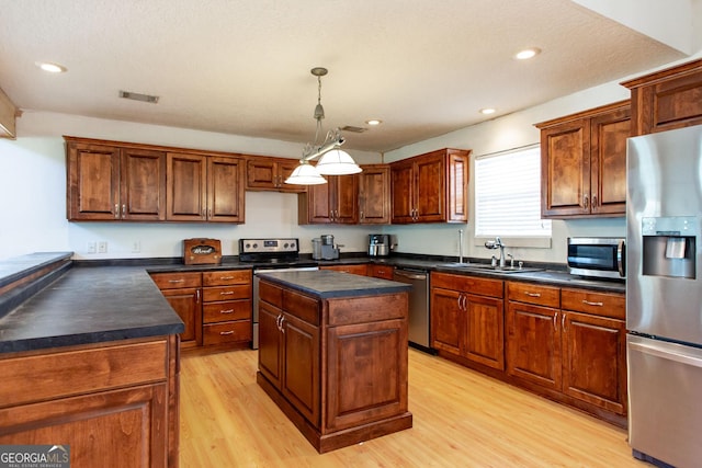 kitchen featuring visible vents, dark countertops, a sink, light wood finished floors, and appliances with stainless steel finishes
