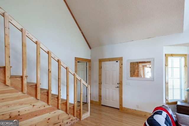 entrance foyer featuring a textured ceiling, light wood-style flooring, stairs, and high vaulted ceiling