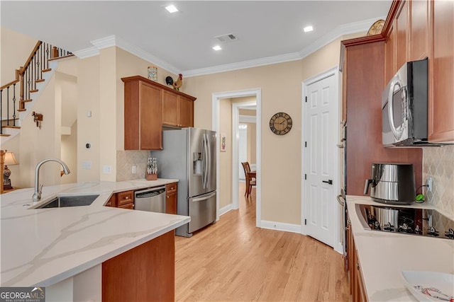 kitchen with backsplash, appliances with stainless steel finishes, brown cabinets, a sink, and light wood-style flooring