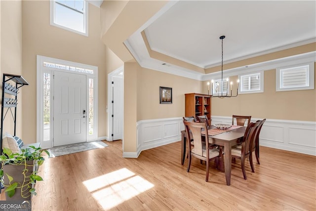 dining space with crown molding, wainscoting, light wood finished floors, a decorative wall, and a chandelier