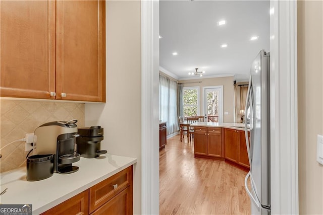 bar featuring freestanding refrigerator, backsplash, crown molding, and light wood finished floors