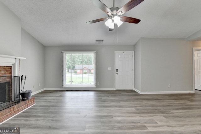 unfurnished living room with visible vents, a brick fireplace, wood finished floors, baseboards, and a ceiling fan