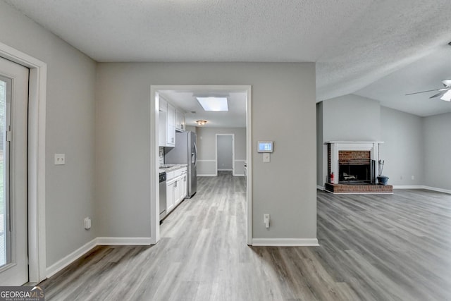 unfurnished living room with ceiling fan, a textured ceiling, a fireplace, baseboards, and light wood finished floors