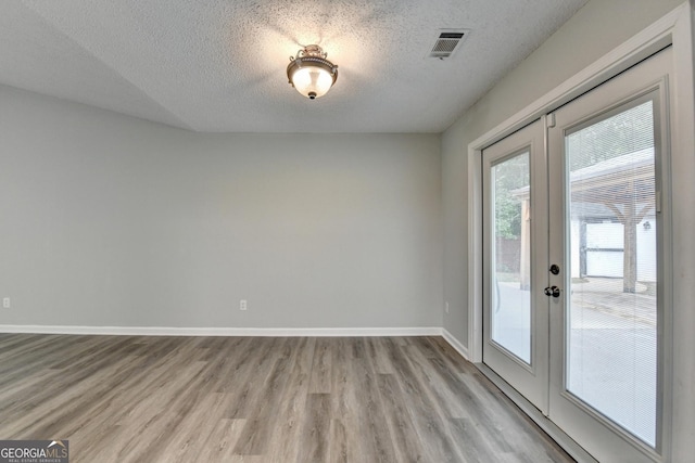 interior space with visible vents, baseboards, light wood-type flooring, a textured ceiling, and french doors