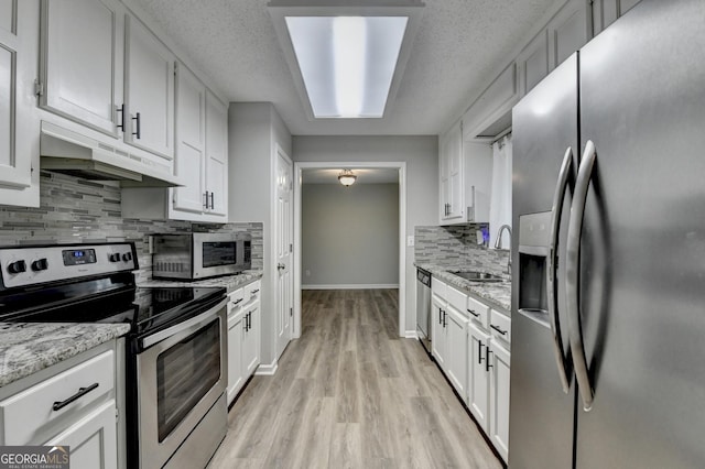 kitchen featuring appliances with stainless steel finishes, a sink, white cabinetry, decorative backsplash, and under cabinet range hood