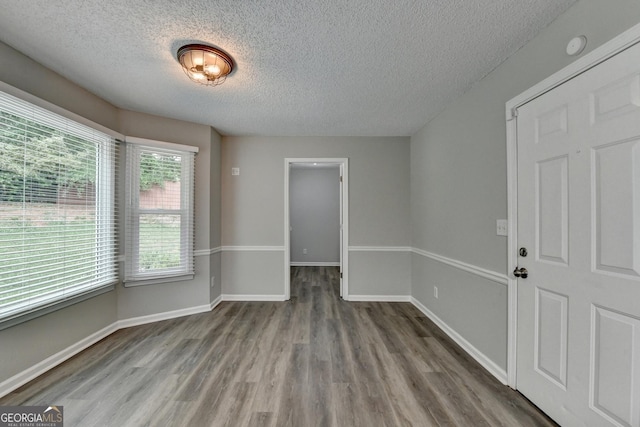 empty room with baseboards, a textured ceiling, and wood finished floors