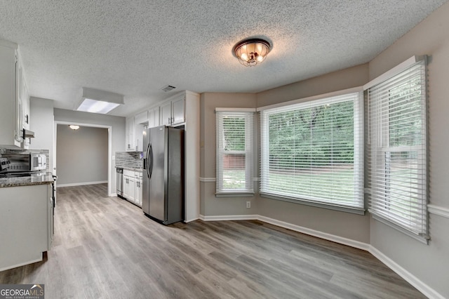 kitchen featuring white cabinets, stainless steel appliances, a textured ceiling, and light wood finished floors