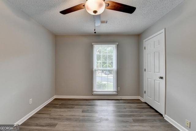 empty room with visible vents, a textured ceiling, ceiling fan, and wood finished floors