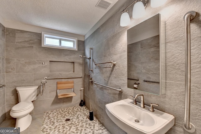 bathroom with visible vents, a sink, tiled shower, and tile walls
