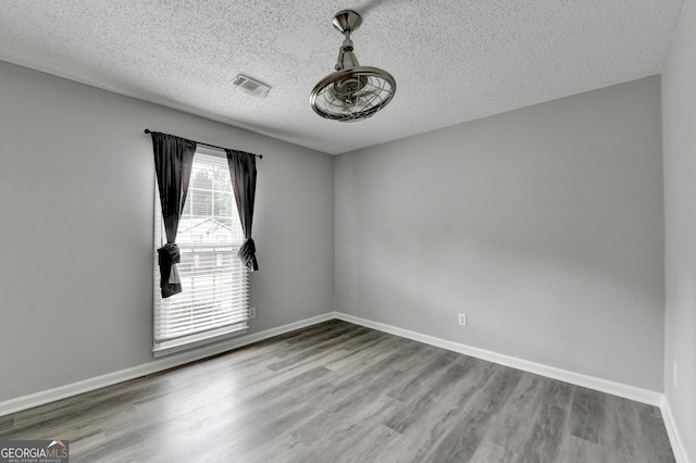 empty room featuring baseboards, visible vents, a textured ceiling, and wood finished floors