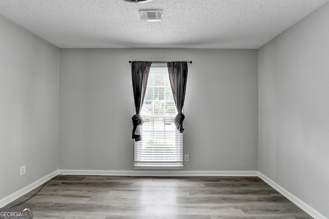 unfurnished room with visible vents, baseboards, a textured ceiling, and wood finished floors