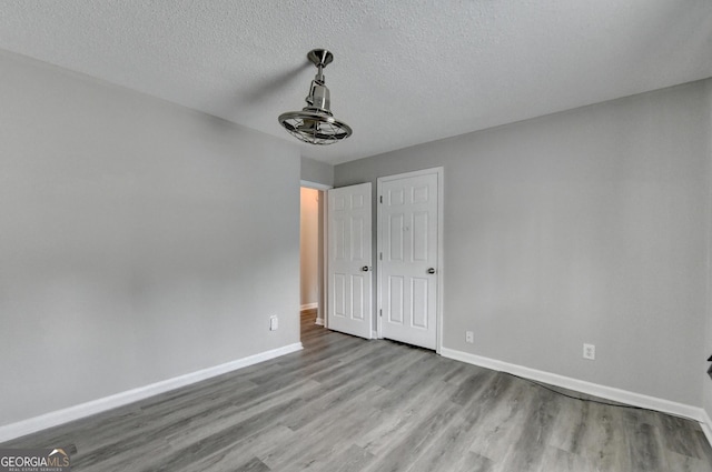 unfurnished bedroom featuring baseboards, a textured ceiling, and wood finished floors