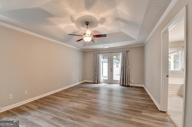 unfurnished room featuring french doors, a ceiling fan, wood finished floors, ornamental molding, and a tray ceiling
