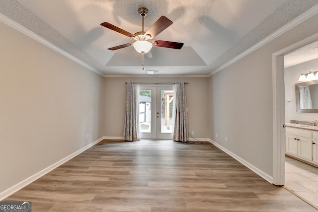 unfurnished room with french doors, a ceiling fan, light wood-style flooring, and a tray ceiling